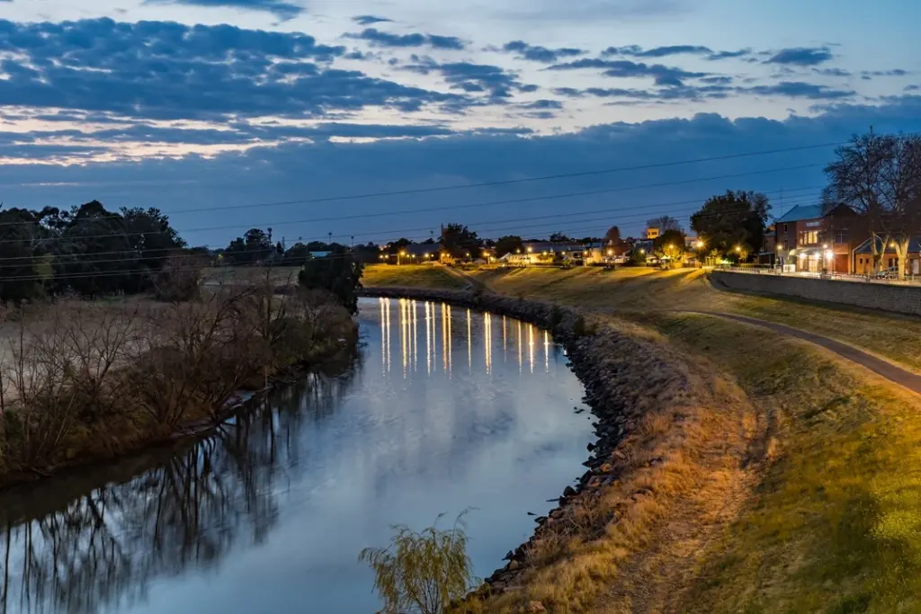 Twilight view of the Hunter river in maitland winding past a suburban area with illuminated homes and paths