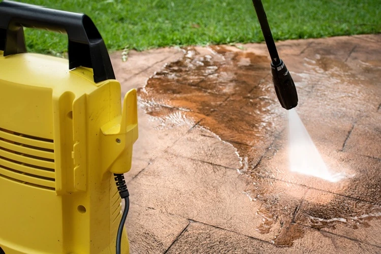 Yellow pressure washer cleaning dirt off a paved patio area with a strong water spray.