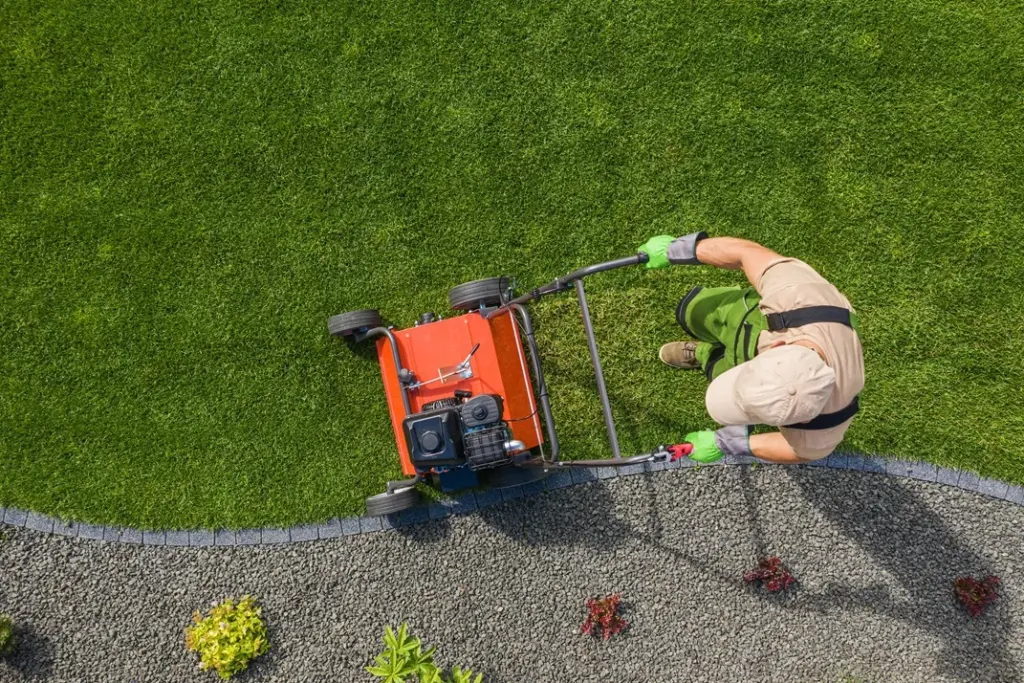 Aerial view of a Lawnmax gardener mowing a curved lawn edge with a red lawn mower alongside landscaped gravel path