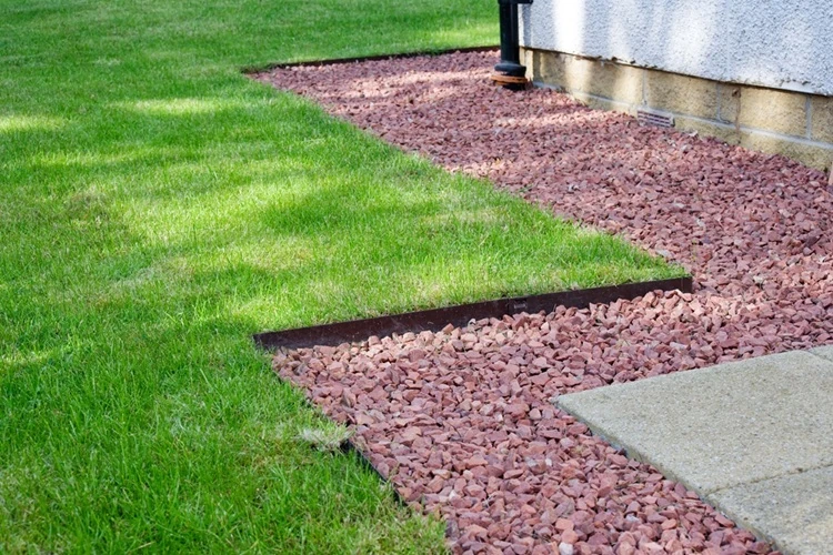 Clean metal edging separating green lawn from reddish gravel mulch beside a house